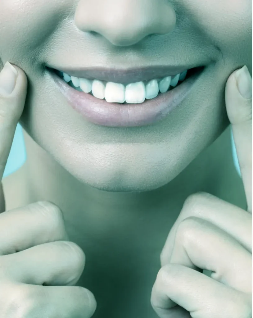 Close-up of a smiling person with their teeth showing, gently touching the corners of their mouth with both index fingers. With a bluish tint, reminiscent of a sleek development platform\'s interface, the image highlights the smile and the smooth skin around the mouth.