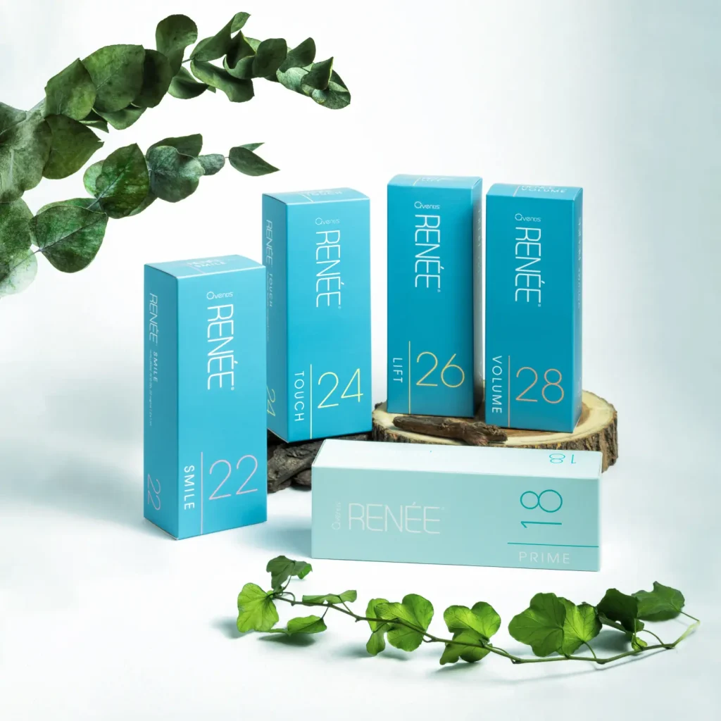 Blue skincare product boxes, associated with medical aesthetics, are displayed on a wooden surface surrounded by green leaves. Each box features numbers and a word, like "Smile 22" and "Volume 28." The scene is set against a light background.