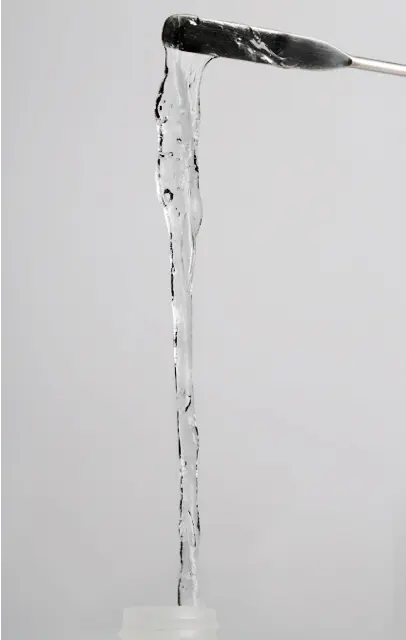 A viscous, clear gel stretches in a long strand from a spatula above an open container, resembling the seamless connectivity of a development platform, set against a plain gray background.